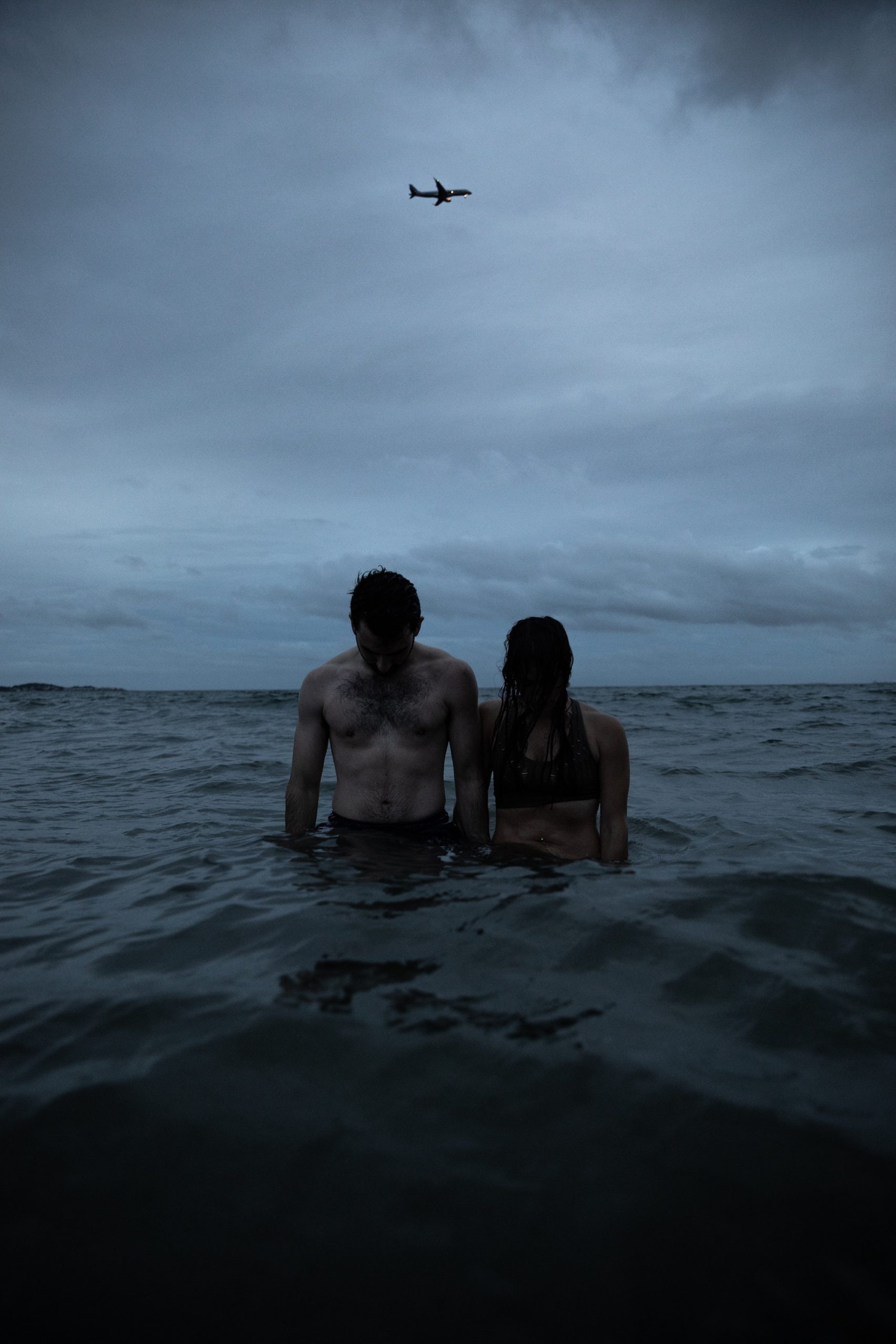 image of a man and woman standing in dark water at the beach on a cloudy day looking down, to showcase the hopelessness of a BPD and narcissist couple